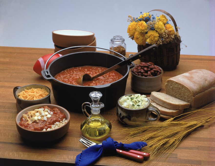 All the items necessary for a chili feast sit on a wooden surface.