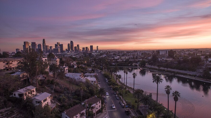 A panoramic view of Los Angeles taken from Echo Park. A skyline of downtown is in the distance, while a large lake is in the foreground. It is sunset.