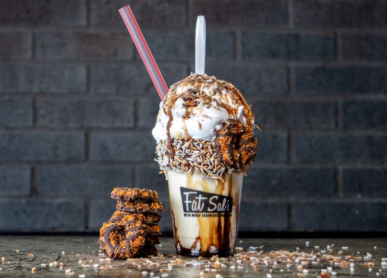 A decadent Samoa shake with ice cream, whipped cream, coconut shavings and samoa cookies in a stack to the left of the shake.