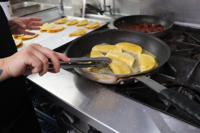 A arm is shown cooking tacos in a frying pan on a stove. 