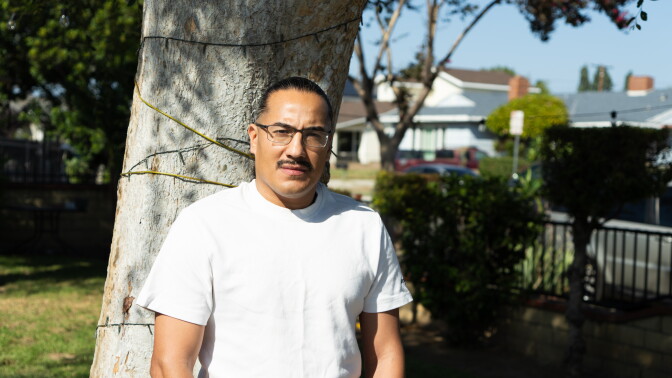 A man stands in front of a tree in a residential neighborhood.