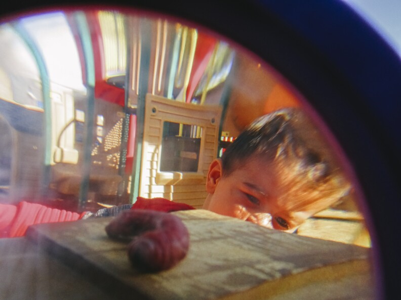 An image shot through a magnifying class with a worm in the foreground and a curious medium skin-toned child's face in the background.