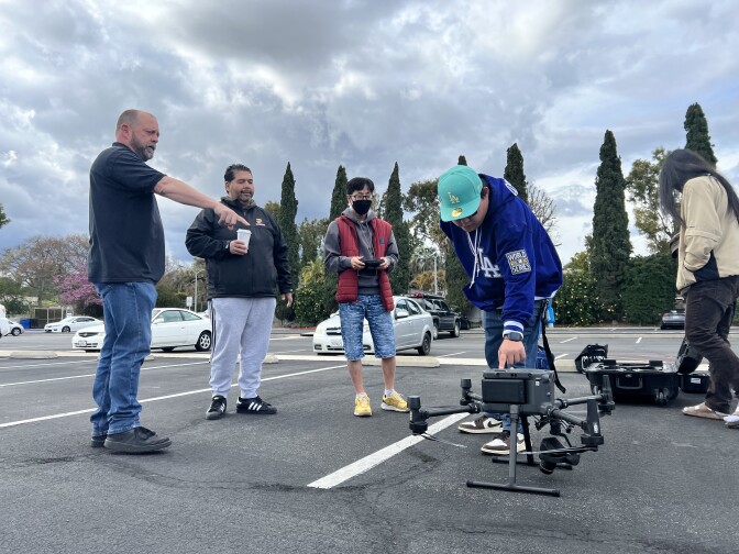 Four Fullerton College students and their professor stand around a gray drone in a parking lot.