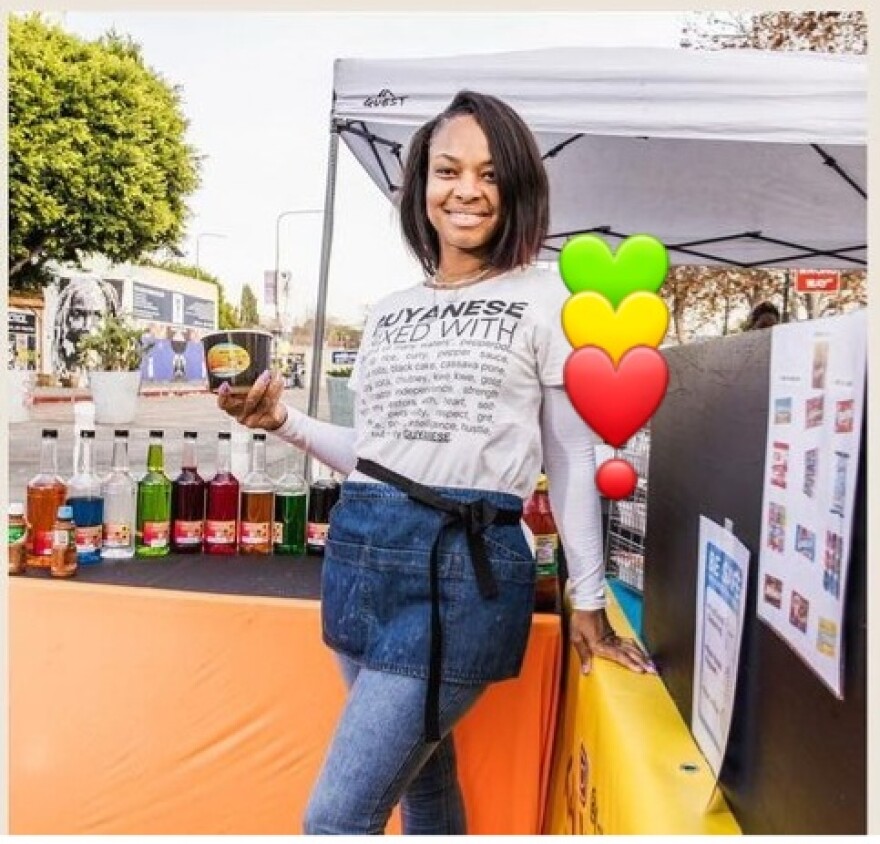 A woman with a shirt that says "Guyanese mixed with..." smiles at the camera as she holds a container of shaved flavored ice.