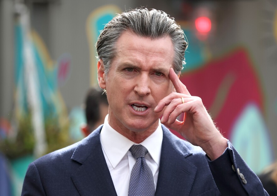 Governor Gavin Newsom touches his temple while speaking.