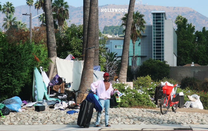 LOS ANGELES, CALIFORNIA - SEPTEMBER 23:  A man stands in front of a homeless encampment, with the Hollywood sign in the background, on September 23, 2019 in Los Angeles, California. A new plan under consideration in the city would bar people experiencing homelessness from sleeping on sidewalks and streets in more than 25 percent of Los Angeles. (Photo by Mario Tama/Getty Images)