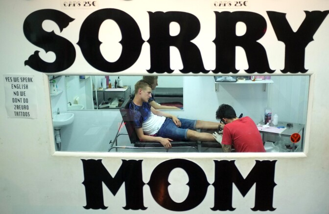 A young British man gets inked at a tattoo parlor of Punta Ballena street, in Magaluf holiday resort, in Calvia on the Spanish Mallorca Island on July 19, 2015.
Known among some tourists as Shagaluf, the resort has suffered particularly bad press over the past 12 months after a video showing a Northern Irish teenage girl performing sex acts on a group of men during a bar crawl went viral last summer. It is estimated 1 million Britons visit the region each year, bringing 800 million euros (866 million dollars)  to the local economy, but the council is desperate to improve the reputation of destination, reported British journal The Guardian. / AFP / JAIME REINA        (Photo credit should read JAIME REINA/AFP/Getty Images)