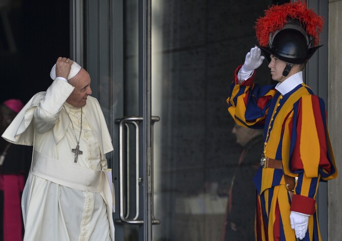 Pope Francis (C) holds his skullcup in front of a Swiss guard as he leaves at the end of the morning session of the Synod on the Families, at the Vatican, on October 6, 2014. Pontiff on Sunday launched a major review of Catholic teaching on the family that could lead to change in the Church's attitude to marriage, cohabitation and divorce. An extraordinary synod, or meeting, of nearly 200 bishops from around the world and a sprinkling of lay people will, for the next two weeks, address the huge gulf between what the Church currently says on these issues and what tens of millions of believers actually do. 