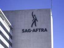 A multi-story stone facade building has SAG- AFTRA on its side with a figure gesturing to the sky