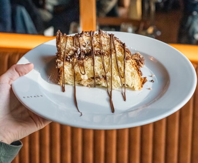 A slice of panettonne on a plate, drizzled with chocolocate sauce. 