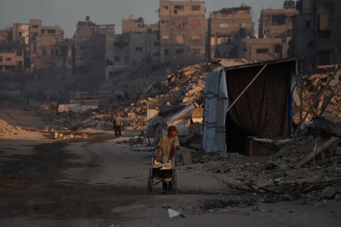 People walks in a street surrounded by the rubble of bombed buildings.