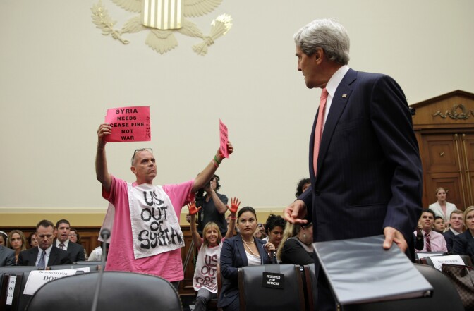 Members of CodePink, Tighe Barry (L) and Medea Benjamin (2nd L) protest as U.S. Secretary of State John Kerry (R) arrives at a hearing on "Syria: Weighing the Obama Administration's Response" before the House Foreign Affairs Committee September 4, 2013 on Capitol Hill in Washington, DC. 