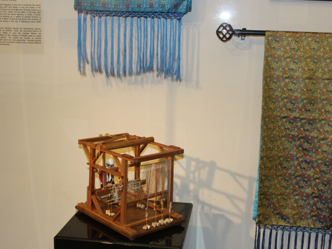 A miniature figurine of a weaver at work on a vertical loom.