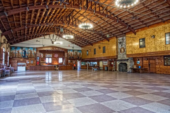 A large lodge has high ceilings, a stage and a large stone fireplace. 