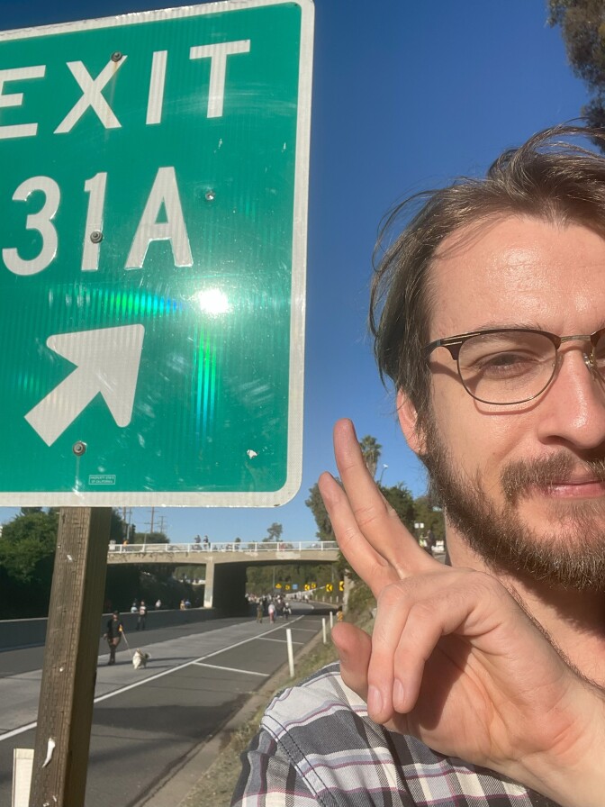 The reporter posing in front of an exit sign and holding up a peace sign.