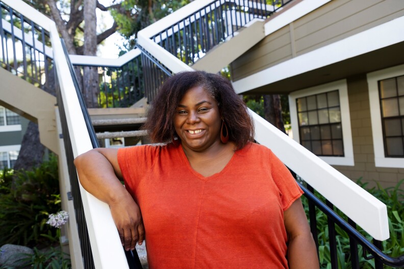 Tamara Fairbanks in an orange shirt and dark hair outside an apartment building.