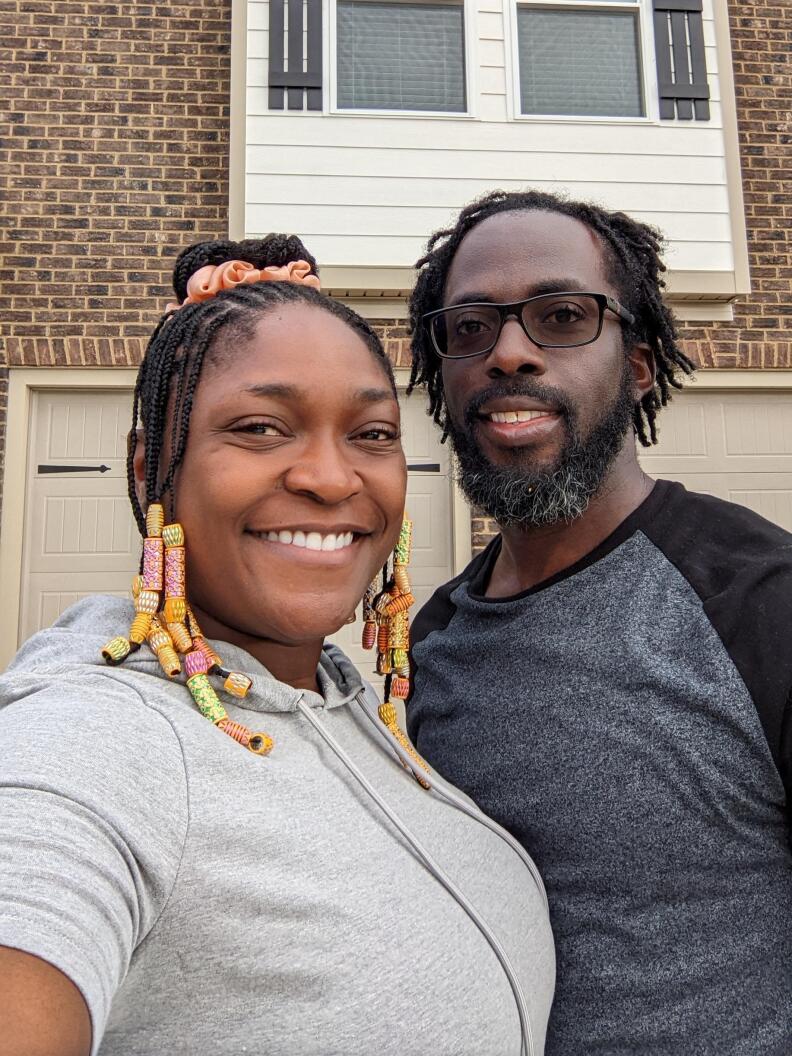 Two people pose in front of a home