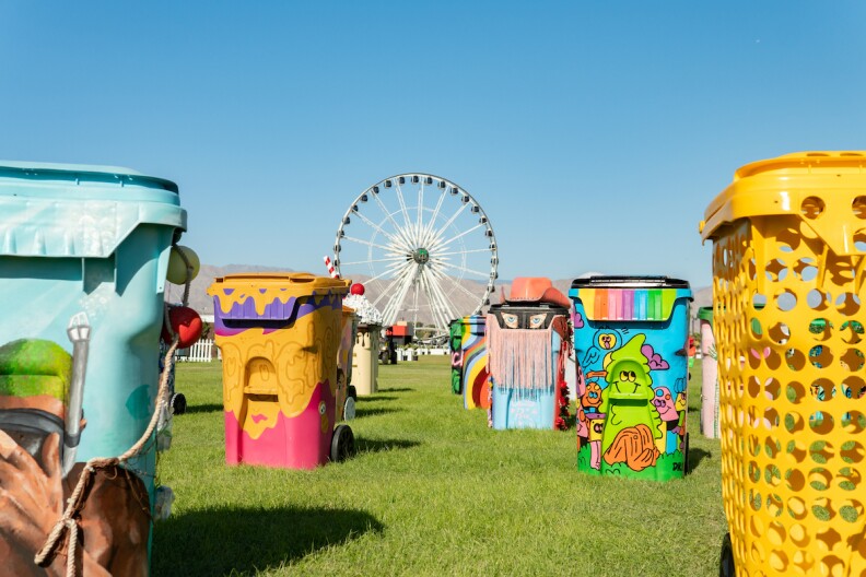 About six artist-designed trash and recycling bins are on a field at Coachella, with the ferris wheel in the background.