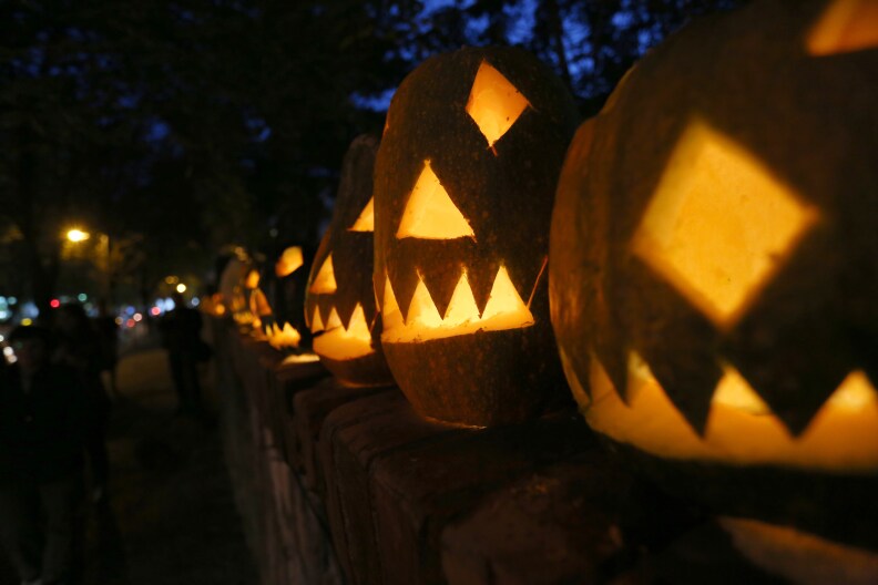 People walk past illuminated and carved pumpkins with grimacing faces on sale, in a street of Tirana on October 30, 2015, one day before Halloween celebration. AFP PHOTO / GENT SHKULLAKU        (Photo credit should read GENT SHKULLAKU/AFP/Getty Images)