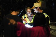 A woman points down the street, showing two people in reflective vests where people have been living on the street.