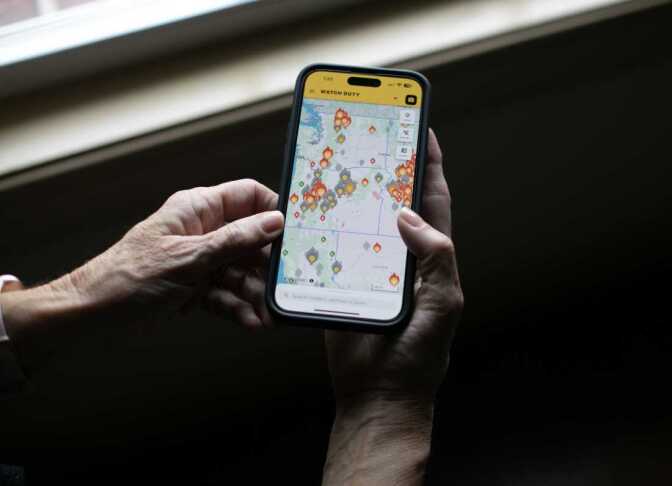 A person's hands hold a phone with flame icons showing the location of fires.