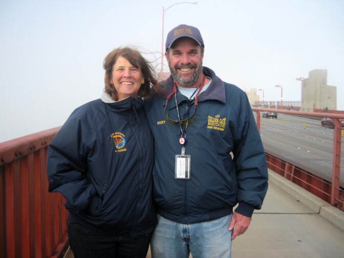 Golden Gate Bridge spokeswoman Mary Currie and paint superintendent Rocky Dellarocca stand on the bridge. The orange cables behind them are obscured by thick fog. From July to October, foghorns blare for more than 5 hours a day on average.
