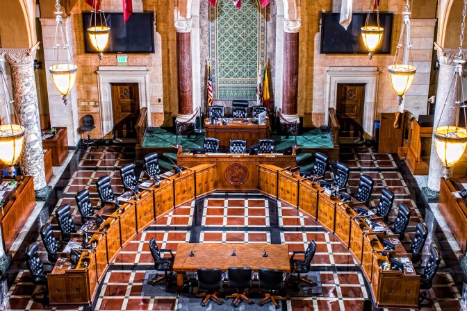 An empty chamber has chairs in a horseshoe shape in an ornate room
