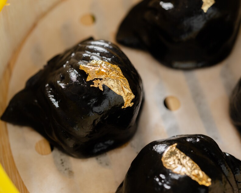 Black squid ink shrimp dumplings with a gold leaf on top of each dumpling.