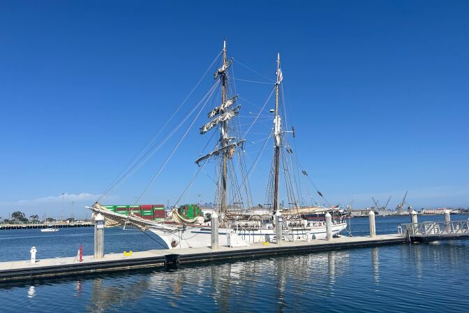 A white sail boats sit off a dock on a bright, sunny day. 