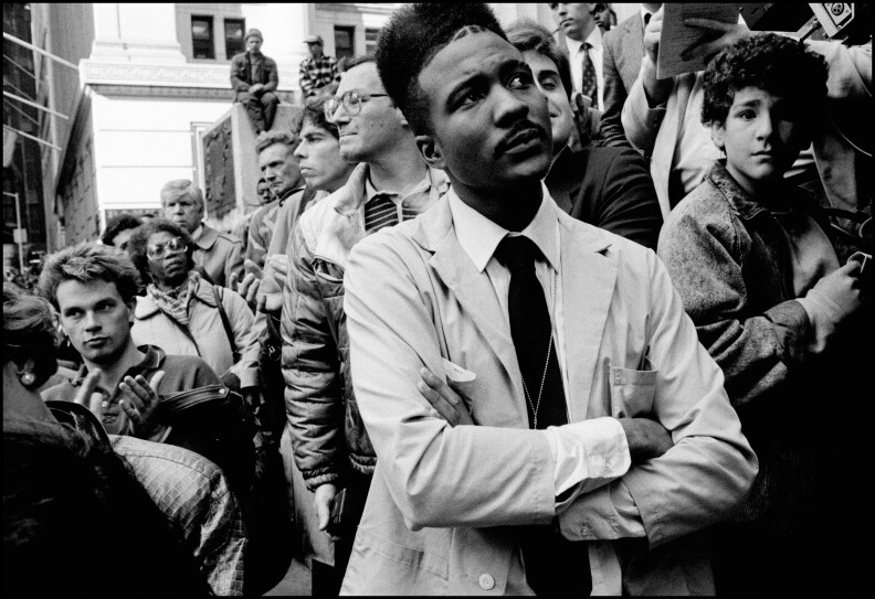 A ma stands with crossed arms on a light-colored suit with a crowd around him