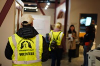 Two people wearing reflective vests walk through a hallway.
