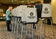 A man with light-tone skin casts a ballot along a row of voting booths
