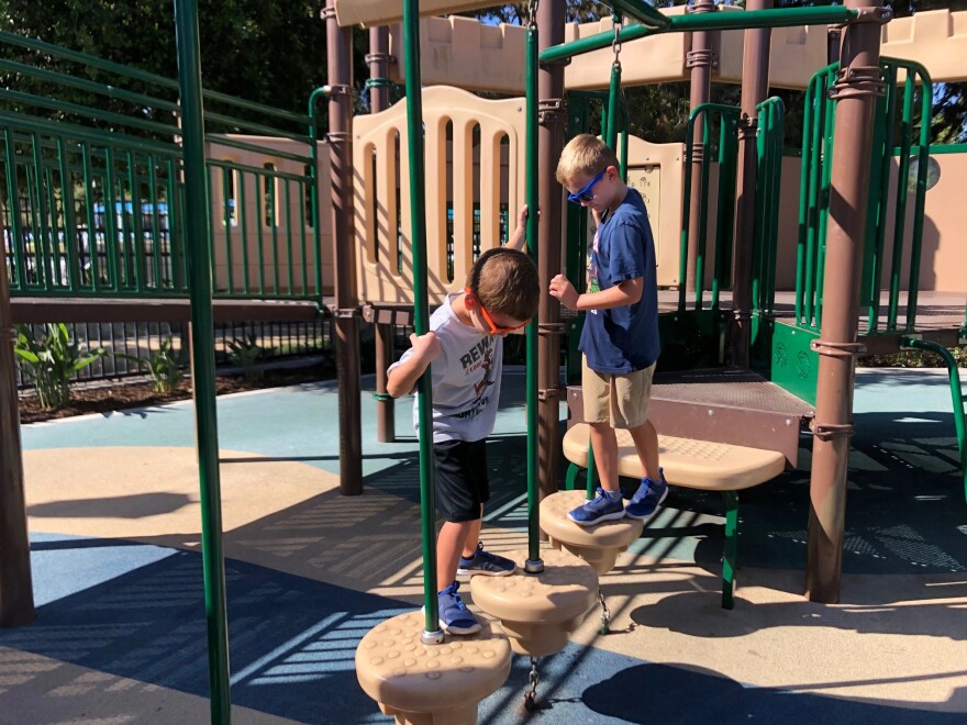 Two kids with glasses play on a playground gym.