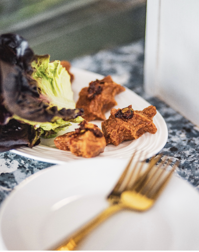 Two small mounds of chi kyuftah, a steak tartare with bulgur and Aleppo pepper, garnished with Aleppo chili crisp and served with red gem lettuce on a white plate.