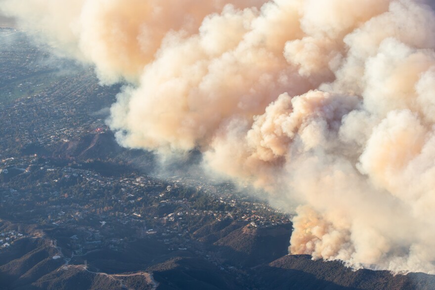 An aerial view of a hilly community partly engulfed in smoke.