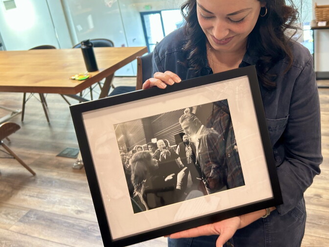 A woman with dark hair holds a framed, black and white photograph and smiles looking down at it.