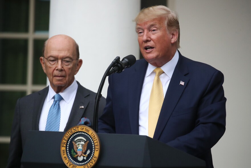 Former U.S. President Donald Trump stands at a lectern next to Wilbur Ross, both men are in suits