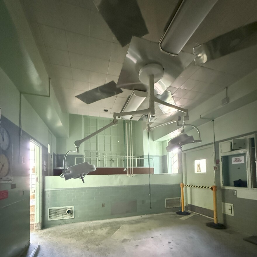 The interior of an operating room at LA County's old General Hospital. The walls are painted pale green. A lighting device is overhead.