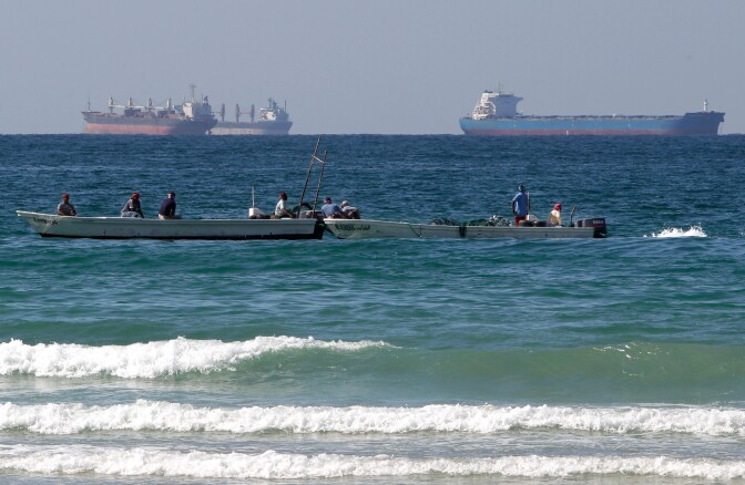 Boats are in ocean waves near large tankers.