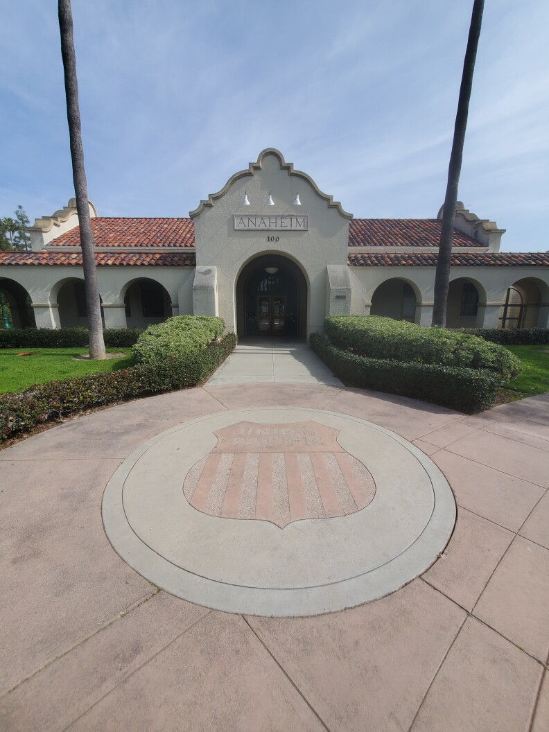 A former train depot turned government building: There is an ornate roofline over the entrance, and that same roof is covered in terra cotta tiles. The sign over the doorway reads "Anaheim."