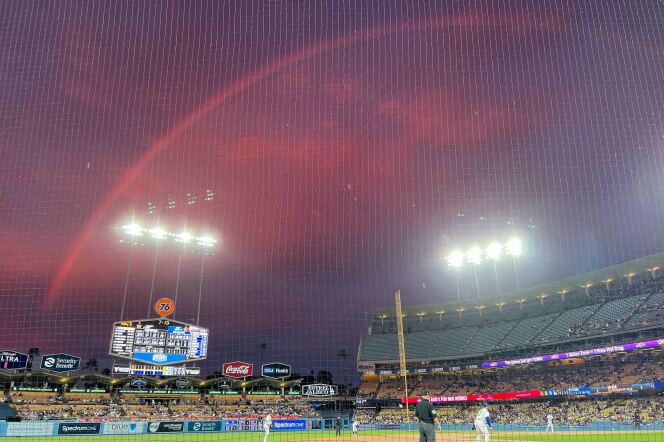 A salmon pink rainbow in a pink hued sky, seen from a baseball field. 