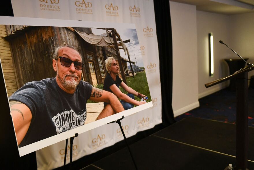 A large-format photo sits on an easel with two people in T-shirts sitting on a Western-style set.