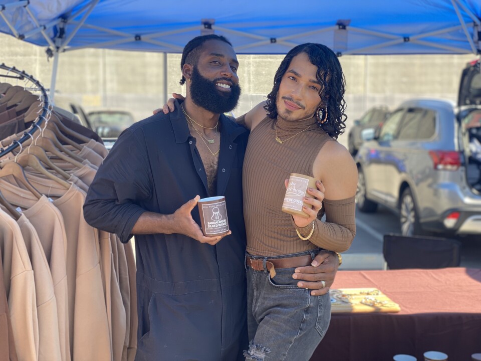 Two vendors, both fashionably dressed, at Queer Mercardo holding their freshly made candles.