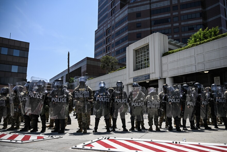 A line of police hold shields. At least two read: California National Guard.