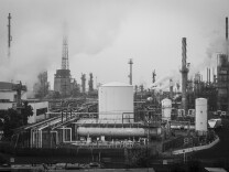 A black and white photo shows the towers and tanks of an oil refinery.