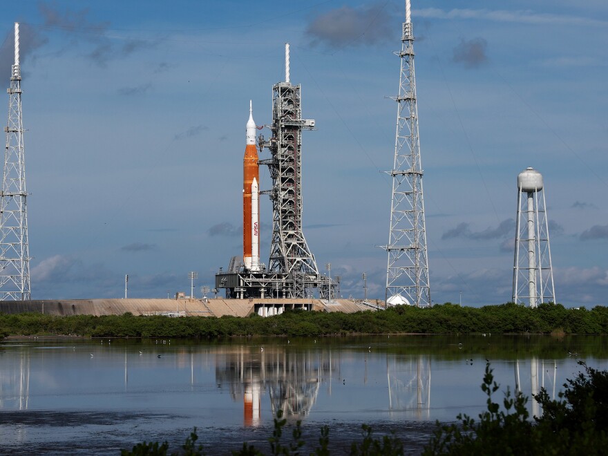 A rocket rests upright at a launching station, the word NASA is visible on its side.