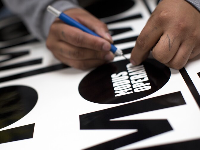 Sign maker Mike Medrano "weeds out" the text for a yellow film set sign on Friday, Jan. 9 at JCL Traffic in Los Angeles.