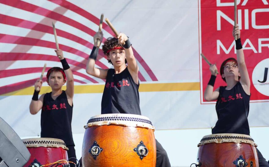3 boys stand behind large taiko drums, their arms in the air, ready to hit the drums with sticks