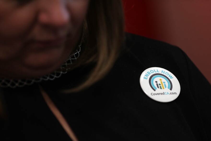 A close-up of a pin on a jacket that reads Enroll Now CoveredCA.com