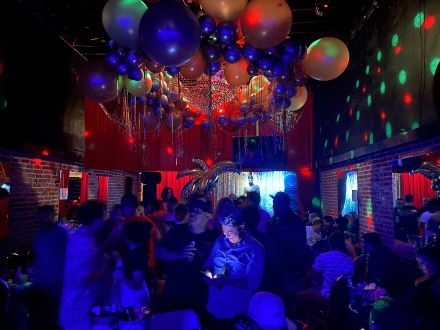 An image of a club filled with people with a ceiling decorated with lights and ballons.
